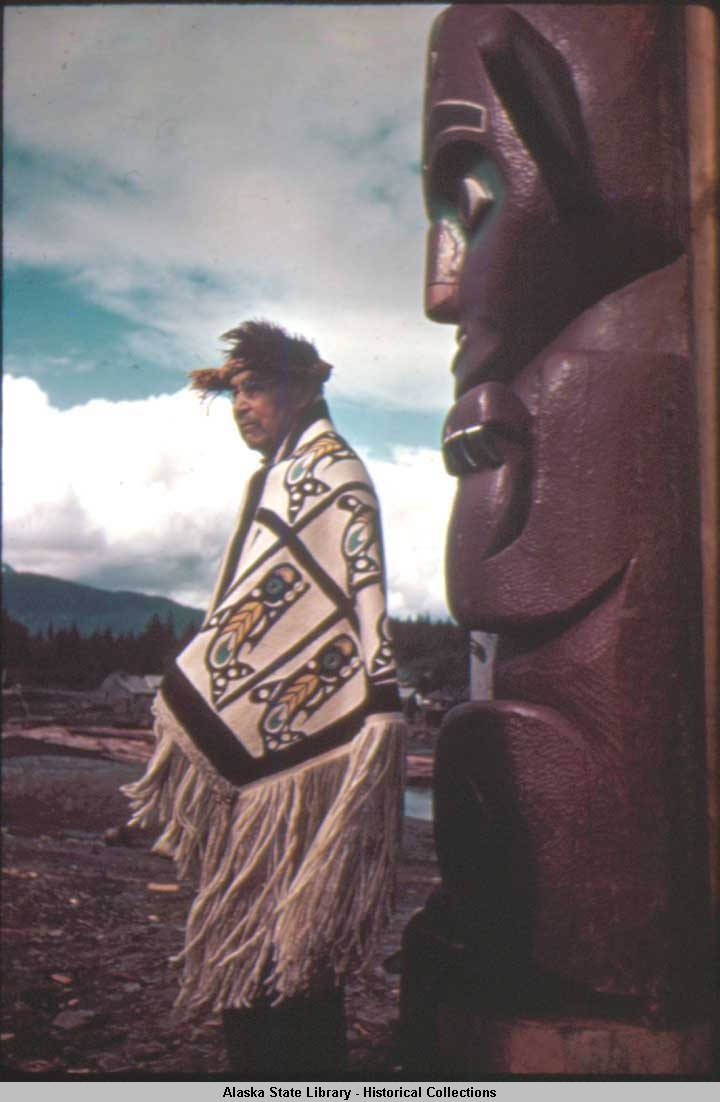 CHIEF IN KILLER WHALE BLANKET STANDING BEFORE HOUSE POST